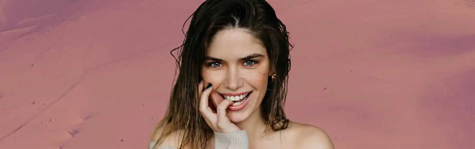 A smiling woman with fresh, glowing skin poses against a soft pink background, highlighting a radiant complexion achieved with the Hydrafacial at Inspire Medical Spa in South Jordan, Utah.